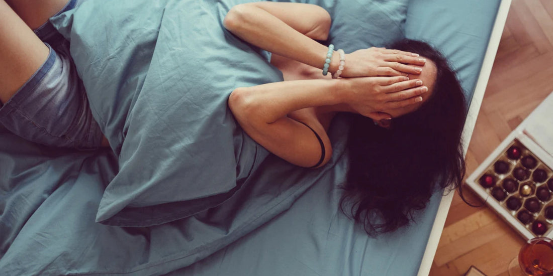 a person lying on a bed, their face covered by their hands