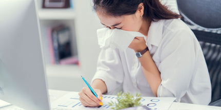 a person in a white shirt blowing their nose with a tissue whilst diligently writing on a paper with diagrams