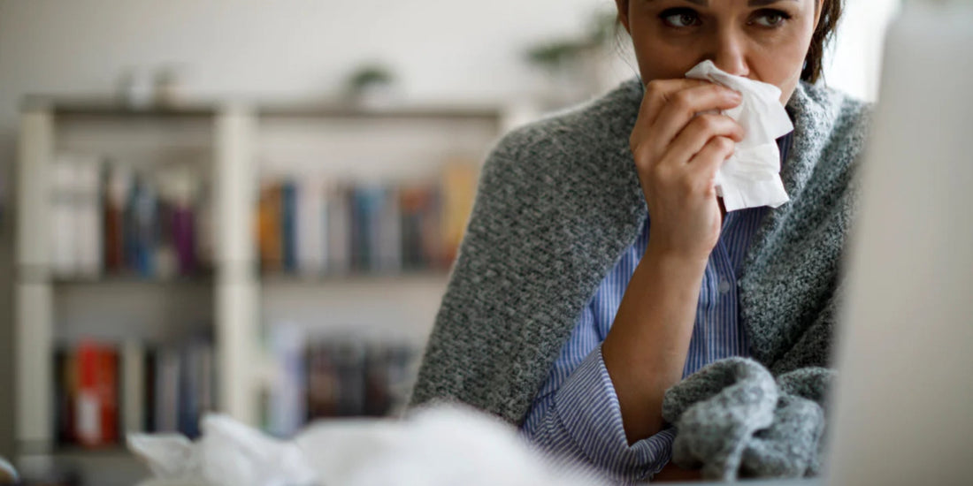 a person sitting at a desk blowing their nose with a tissue