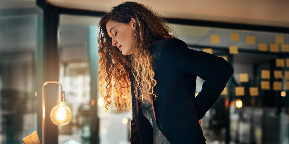 a tired woman standing up straight holding her lower back in pain