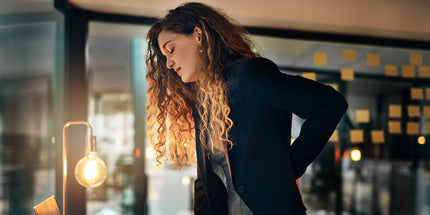 a tired woman standing up straight holding her lower back in pain