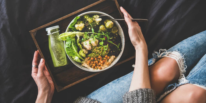 a person holding a tray with a bowl of fresh salad and a bottle of green juice