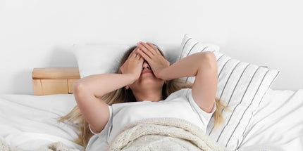 a person laying in their bed with their hands covering their face
