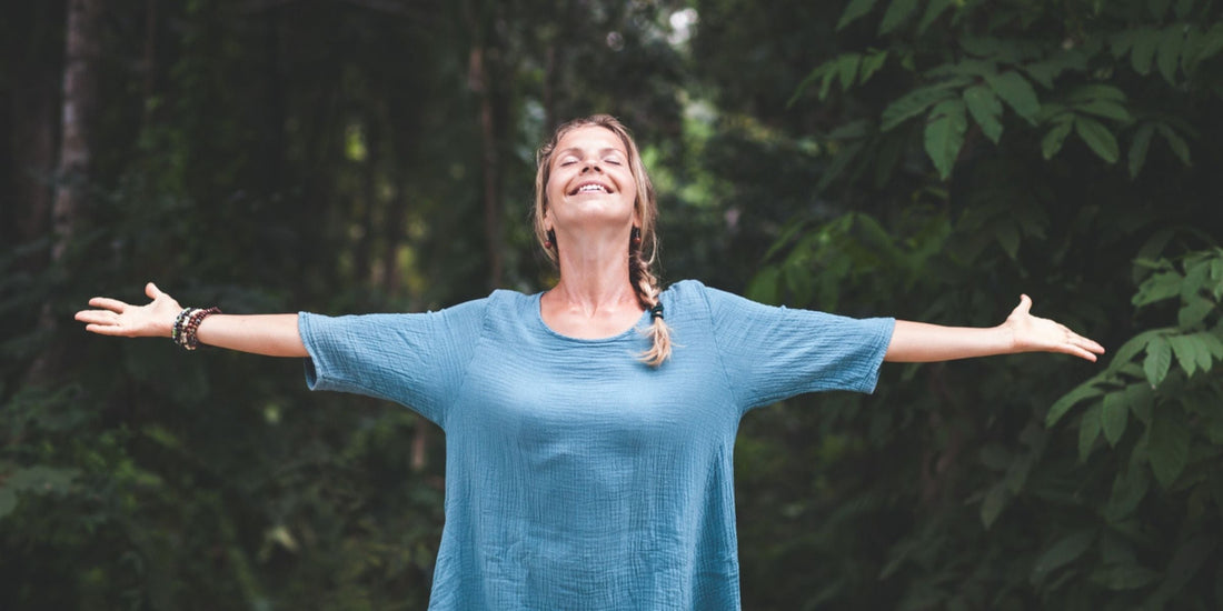 a mature woman standing outside and basking in the sunlight with arms wide