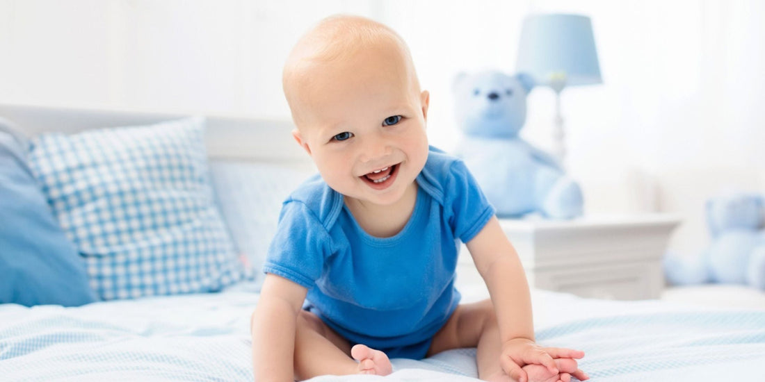 a baby sitting on a bed with a blue onesie