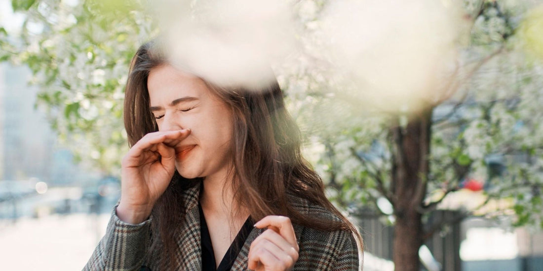 Woman with a bag over her shoulder standing on the side of the street and sneezing during spring time