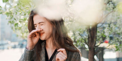 Woman with a bag over her shoulder standing on the side of the street and sneezing during spring time