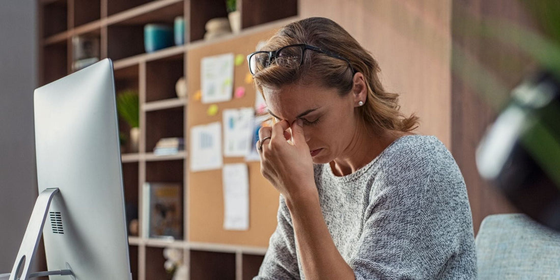 Stressed woman at computer pinching the bridge of her nose in frustration
