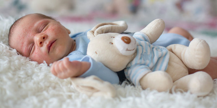 A baby lying next to a plush bear toy on a soft, fluffy blanket