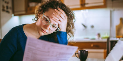 A person in a blue sweater, holding papers, with a blurred kitchen background