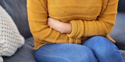 woman wearing a yellow sweater and sitting on a couch holding her arms around her stomach