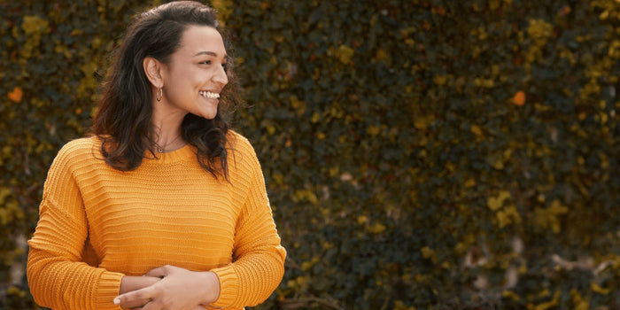 Happy woman holding her stomach and standing against a tall hedge
