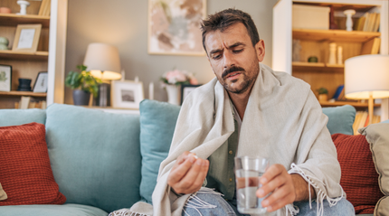 Unwell man sitting on couch taking supplements