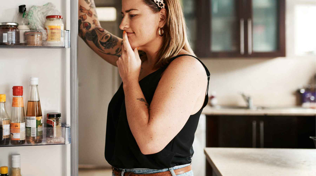 Woman considering appetite and hunger infront of an open fridge door.