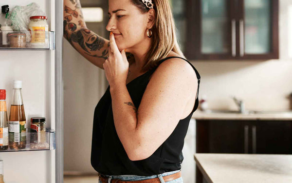 Woman considering appetite and hunger infront of an open fridge door.