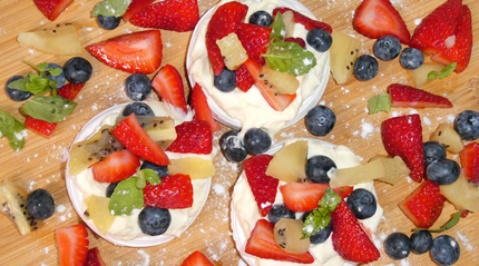 Three mini pavlova's plated on a wooden chopping board.
